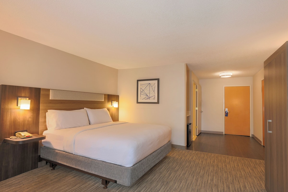 A hotel room with a bed, bedside table, lamp, and a framed picture on the wall.