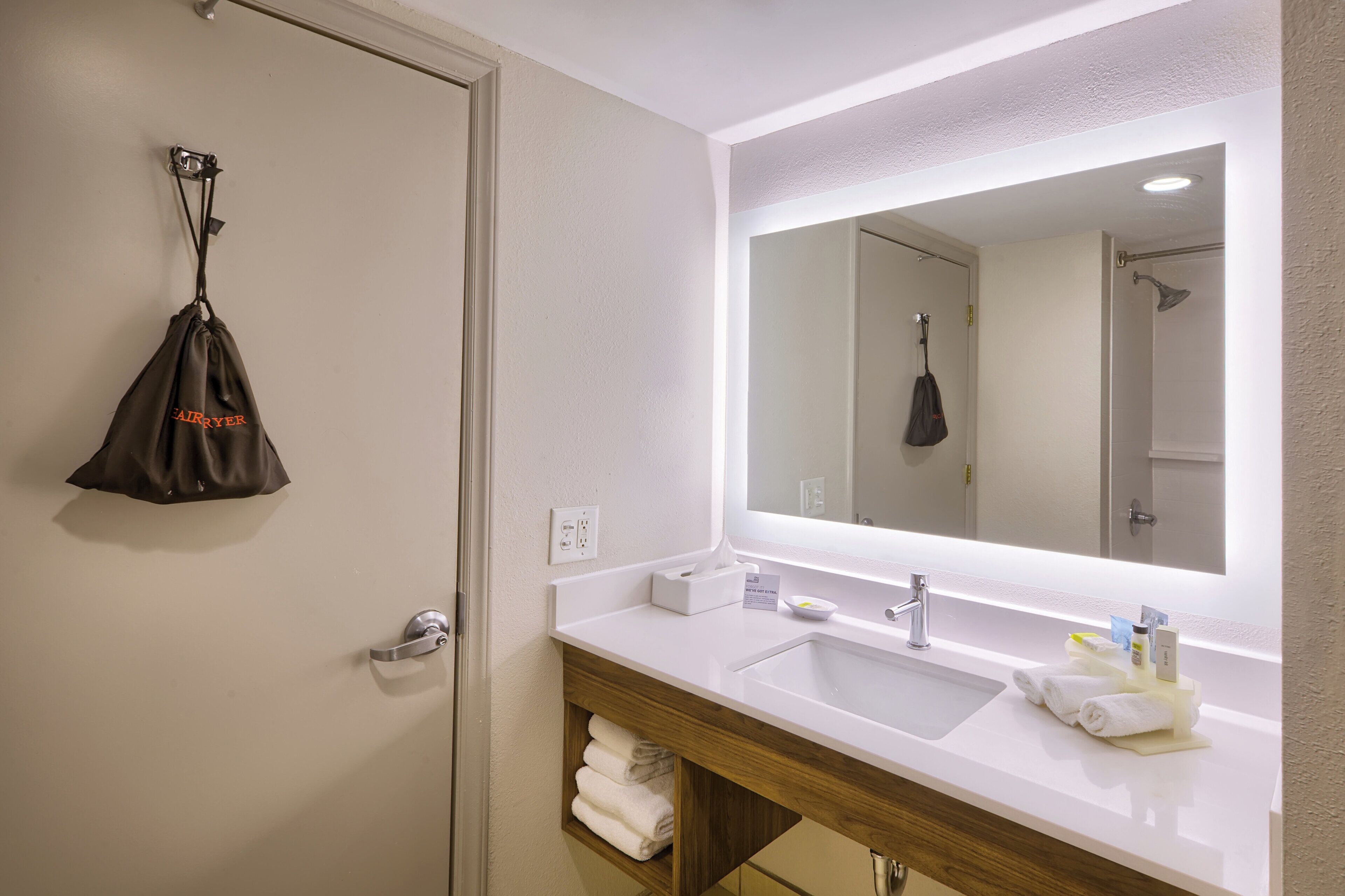 A hotel bathroom with a large mirror, a sink, a towel rack, and a shower area.