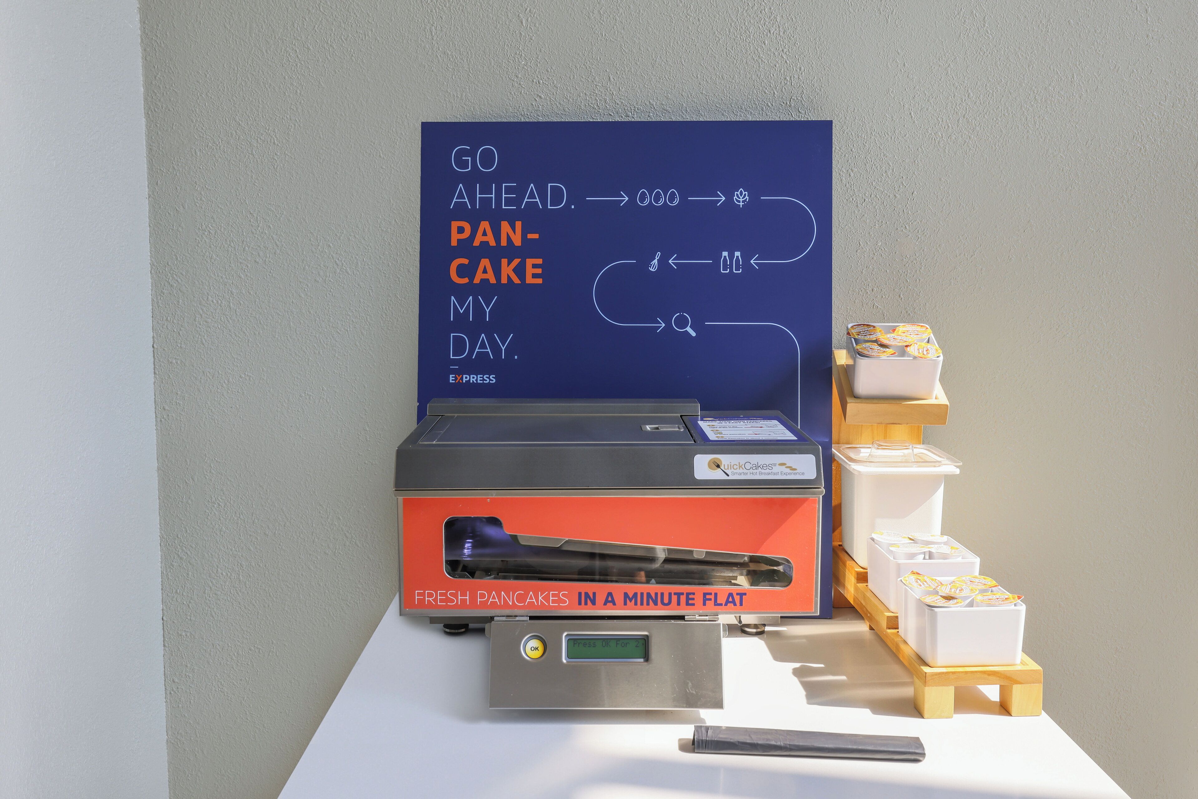 A breakfast setup with a sign that reads "GO AHEAD PANCAKE MY DAY" and a machine for making pancakes.