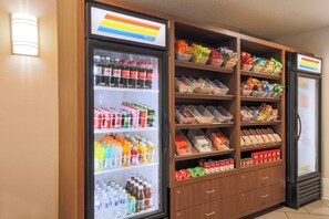 A vending machine stocked with beverages and snacks, including Coca-Cola and various other drinks and packaged foods.