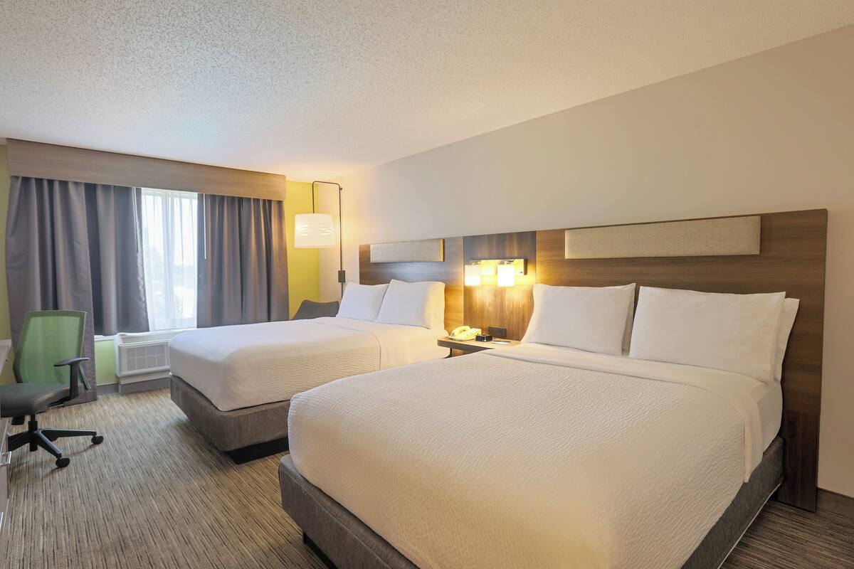 A hotel room with two beds, a desk, a chair, and a lamp.