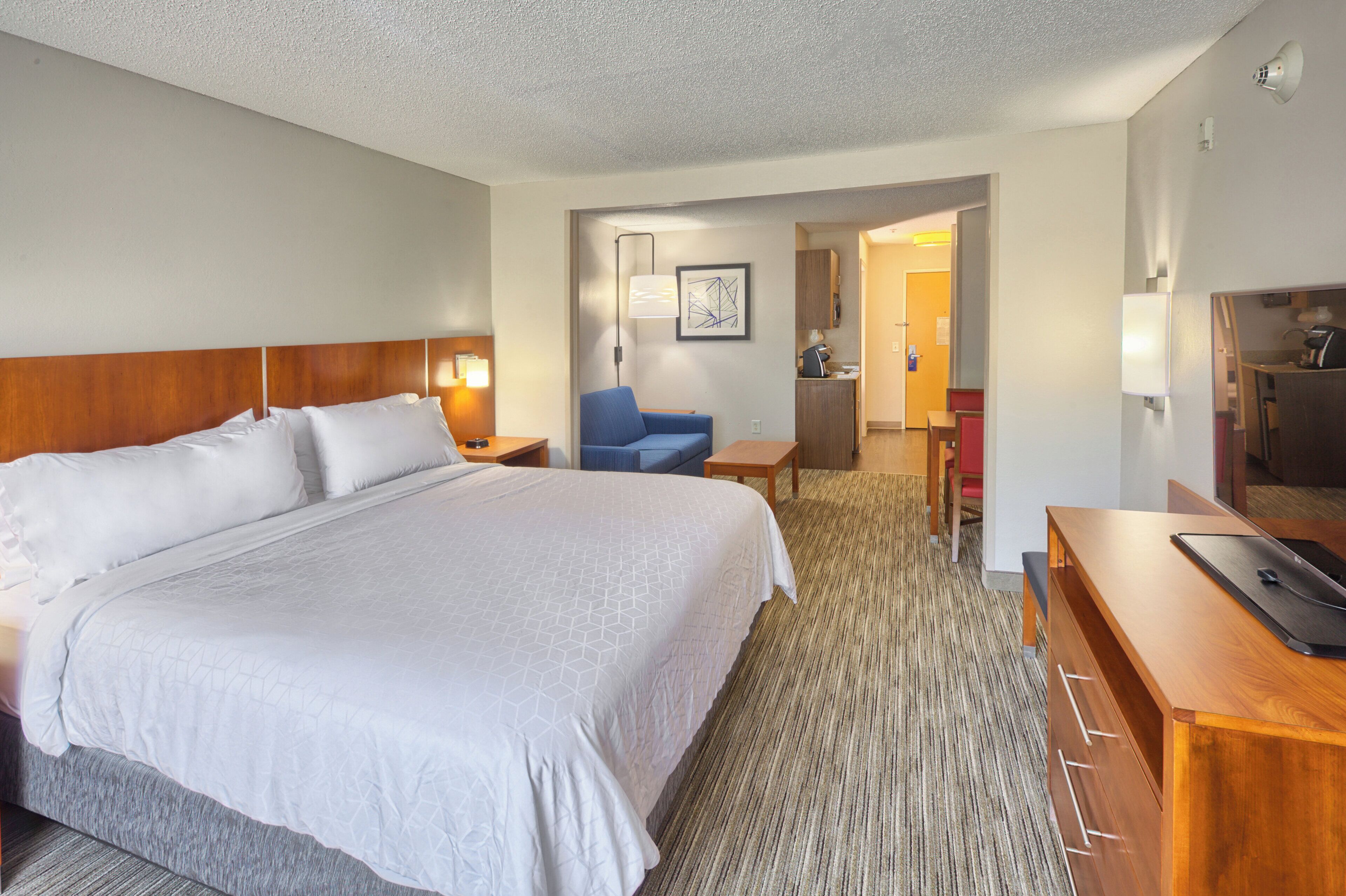 A hotel room with a large bed, a desk, a chair, and a kitchenette.