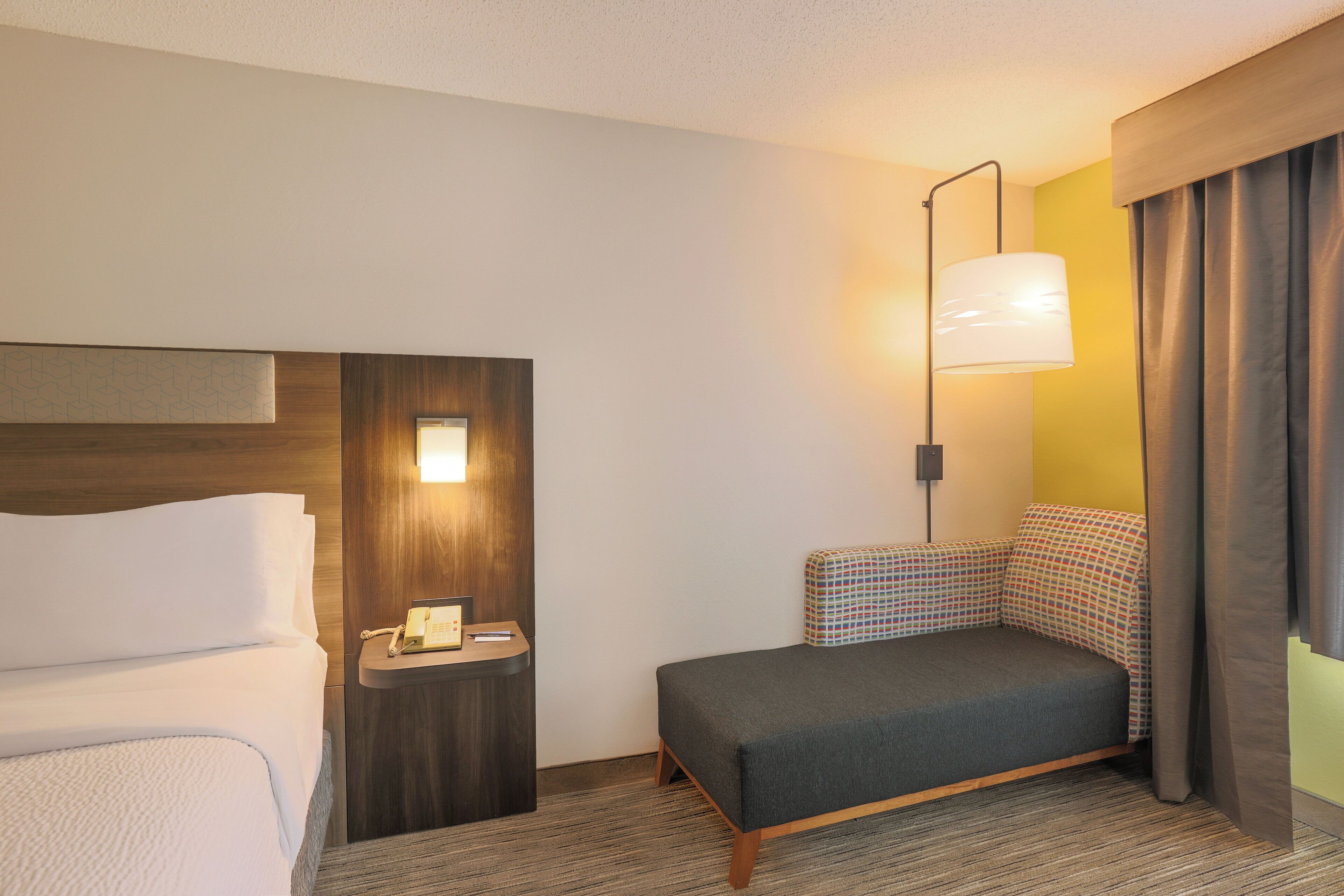 A hotel room with a bed, a bedside table with a telephone, a lamp, and a sofa.