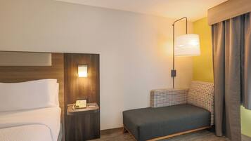 A hotel room with a bed, a bedside table with a telephone, a lamp, and a sofa.