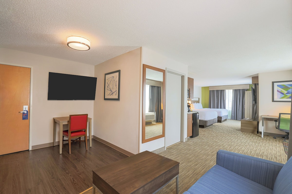A hotel room with a wooden desk, a blue sofa, a bed, a TV, and a mirror.