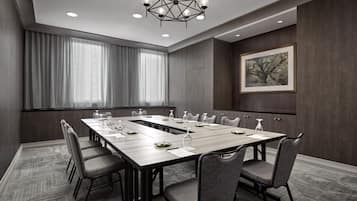 A conference room with a long table, chairs, a chandelier, and a painting on the wall.