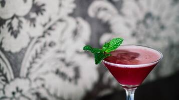 A martini glass with a red drink and a mint garnish on a table.