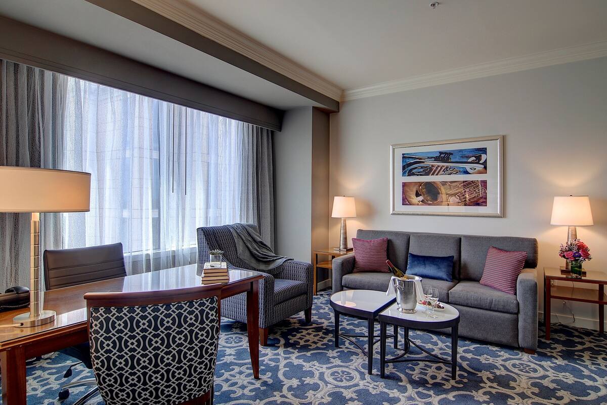 Ein Hotelzimmer mit Esstisch, zwei Sesseln, einer Couch, einem Couchtisch und einem Bild an der Wand.