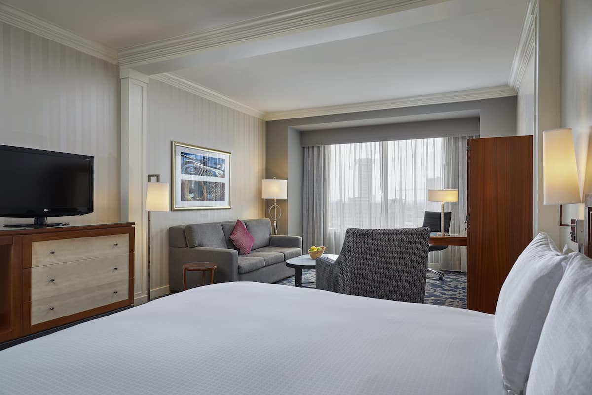 Ein Hotelzimmer mit einem großen Bett, einem Fernseher, einer Couch, einem Sessel, einem kleinen Tisch und einem Schreibtisch mit einer Lampe.