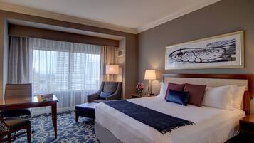 Ein Hotelzimmer mit einem großen Bett, einem Schreibtisch, einem Stuhl und einem Fenster mit Vorhängen.