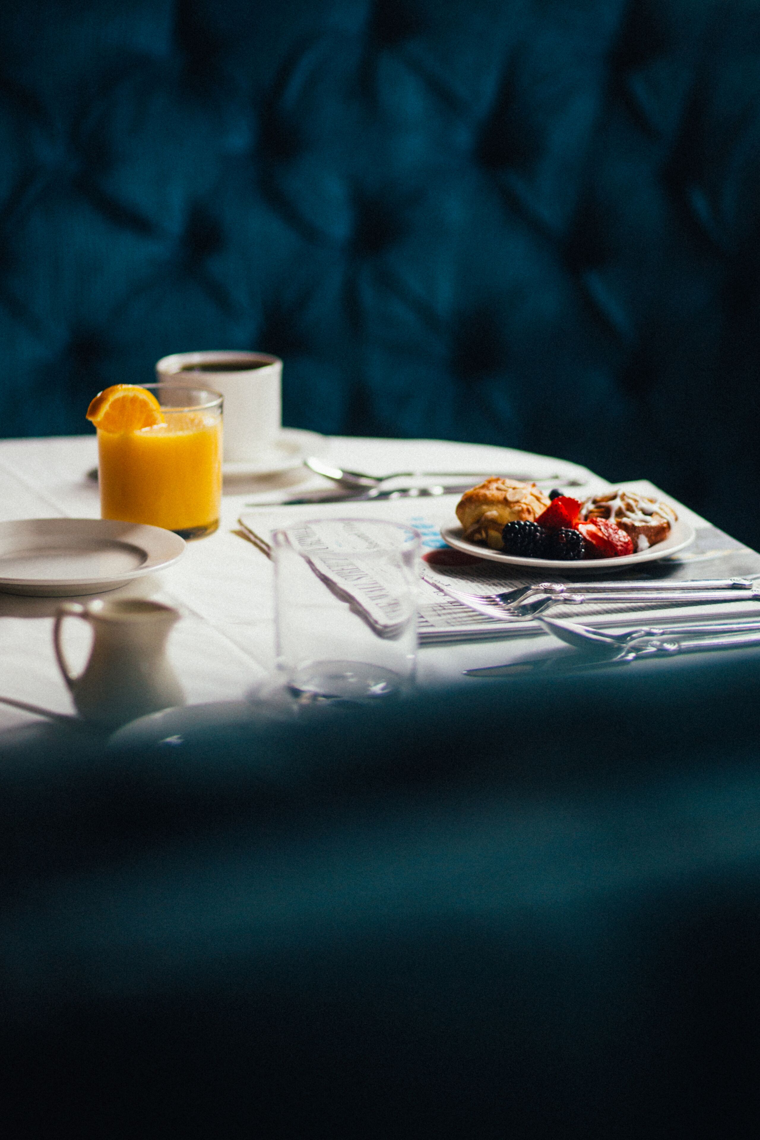 A breakfast setting with a plate of pastries, a glass of orange juice, and a cup on a table with a white tablecloth.