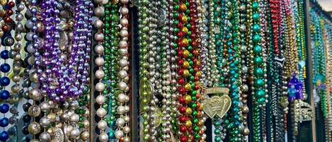A row of colorful beaded necklaces displayed outside a building with a green window and a black fence.