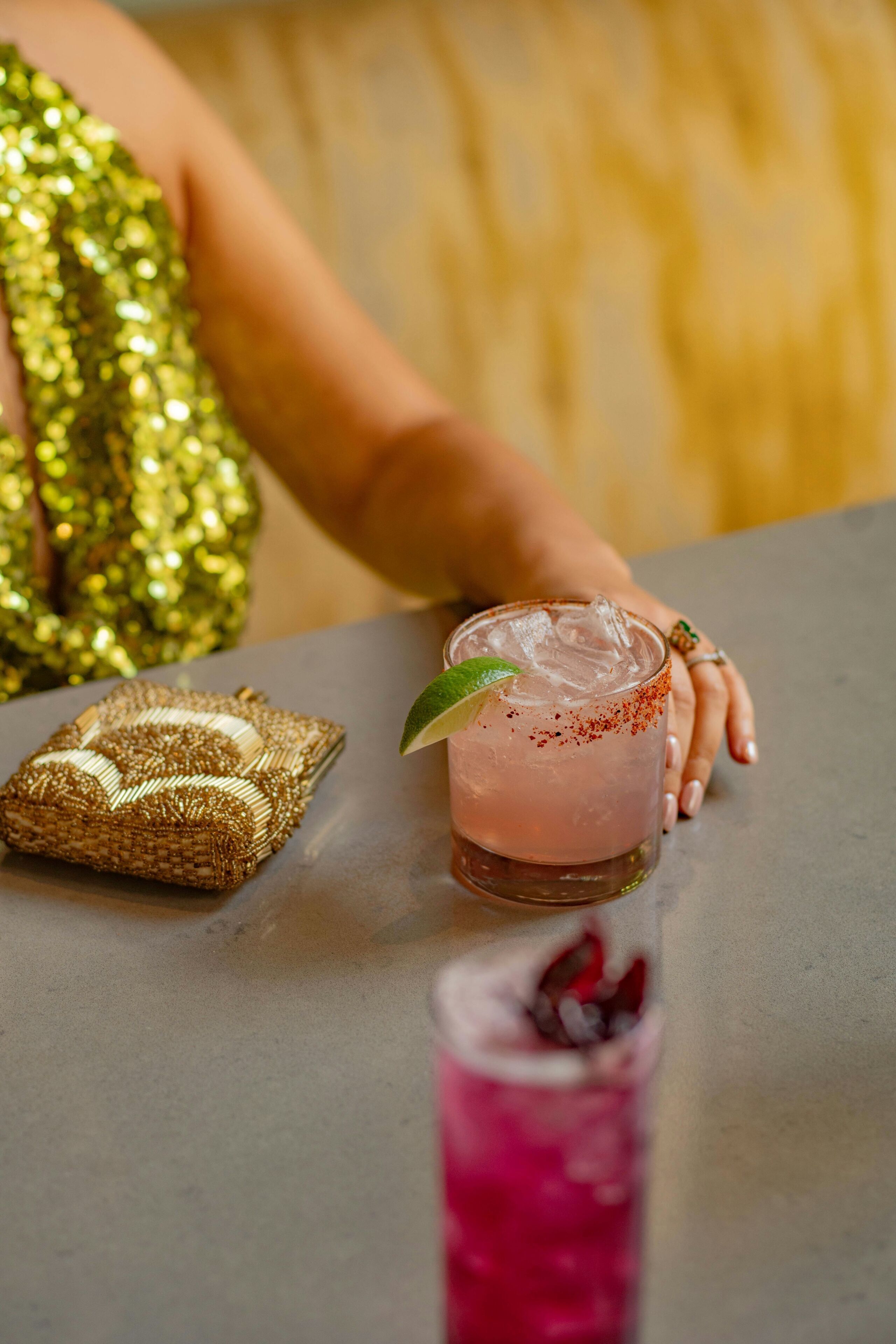Una mesa con una bebida, una pequeña bolsa tejida y la mano de una persona.