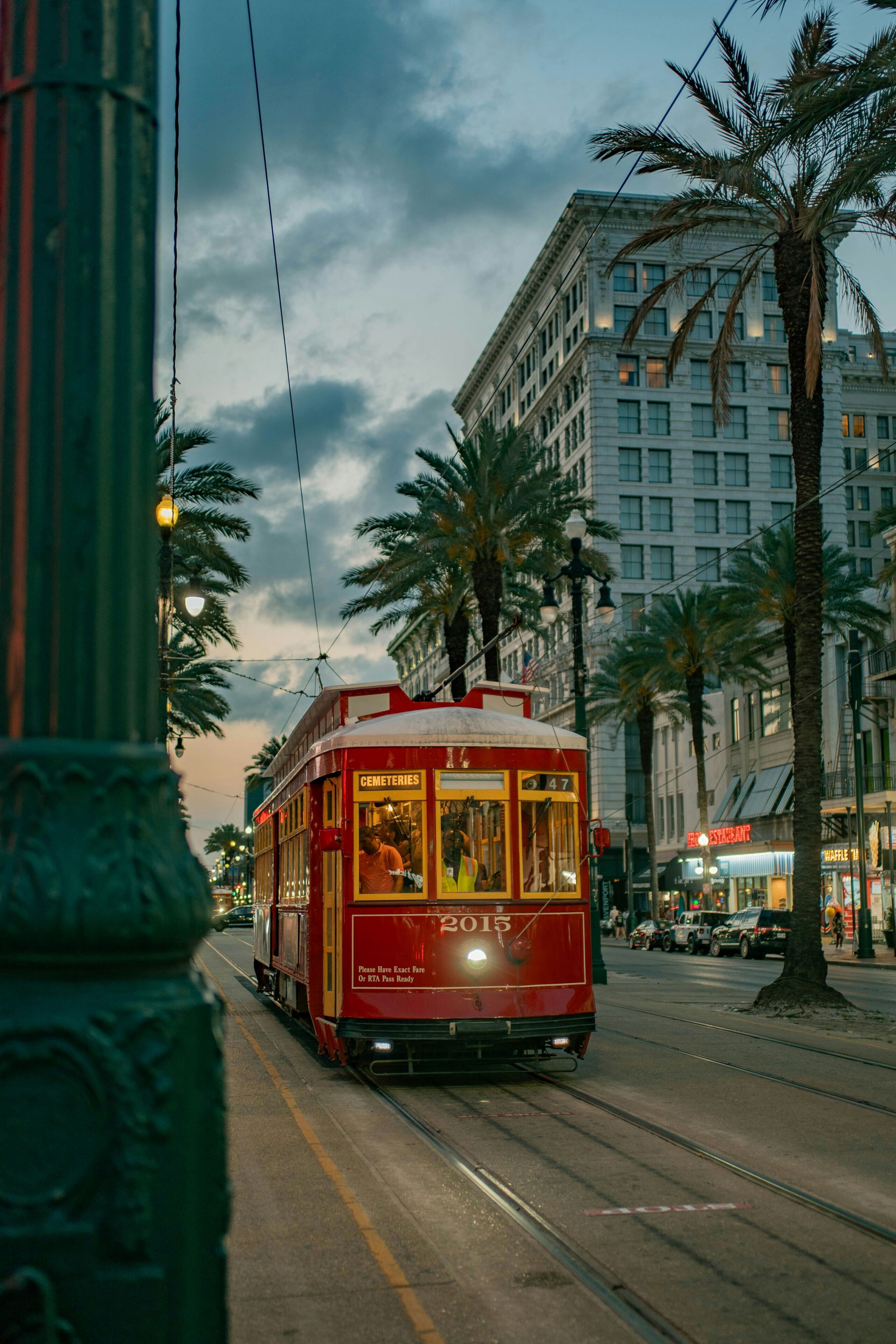 A red trolley on a street with buildings and palm trees in the background.