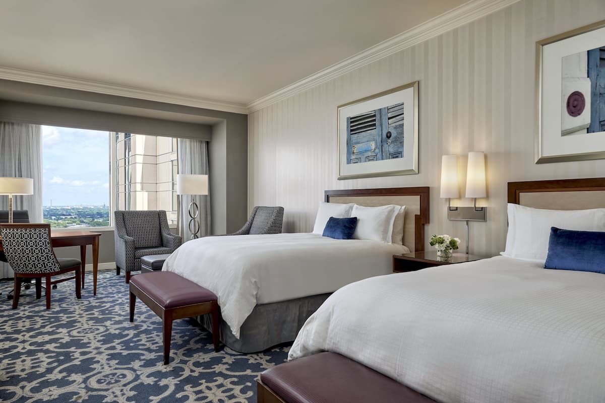 Ein Hotelzimmer mit zwei Betten, einem Schreibtisch, einem Sessel und Blick auf die Stadt.