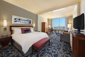 Ein Hotelzimmer mit einem großen Bett, einem Schreibtisch, einem Fernseher und Blick auf die Stadt.