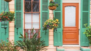 A building with green shutters, a central window, and a door with a white panel. There are hanging flower baskets and potted plants in front. - Loews New Orleans Hotel (New Orleans)