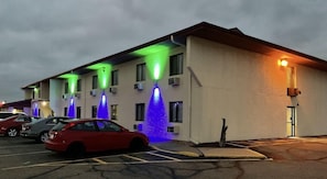 Ein mehrstöckiges Hotel mit Parkplatz, ausgestattet mit einer Reihe beleuchteter Säulen und einem roten Auto im Vordergrund.