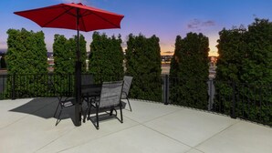 An outdoor patio with a table and chairs, a red umbrella, and a view of trees and a sunset. - Super 8 by Wyndham Winona MN (Winona)