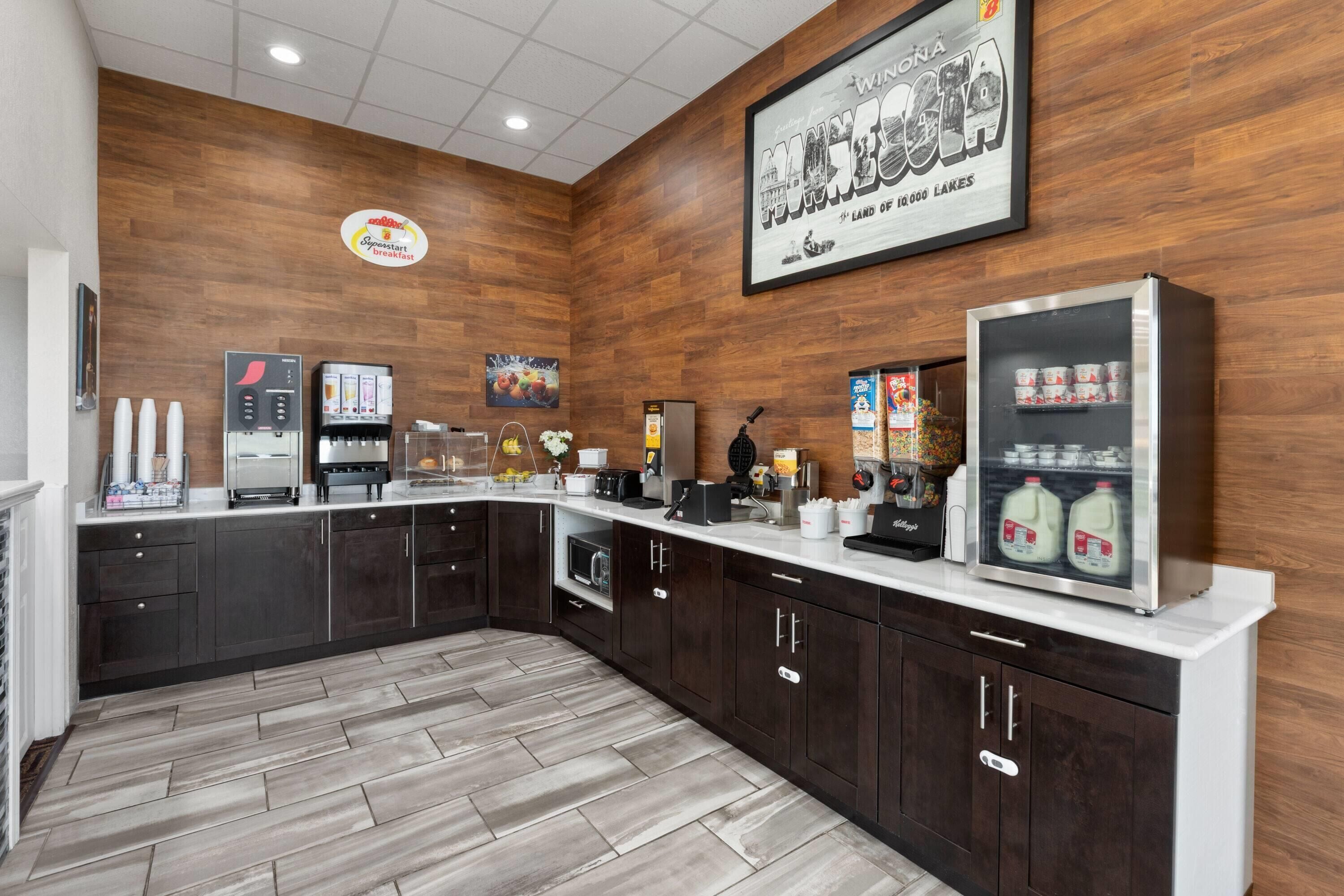 Una cocina moderna con armarios de madera oscura, encimera blanca y diversos electrodomésticos, incluyendo una cafetera y un refrigerador.