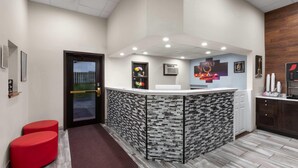 A reception area with a modern design, featuring a check-in counter, a door, and a small seating area with red stools. - Super 8 by Wyndham Winona MN (Winona)