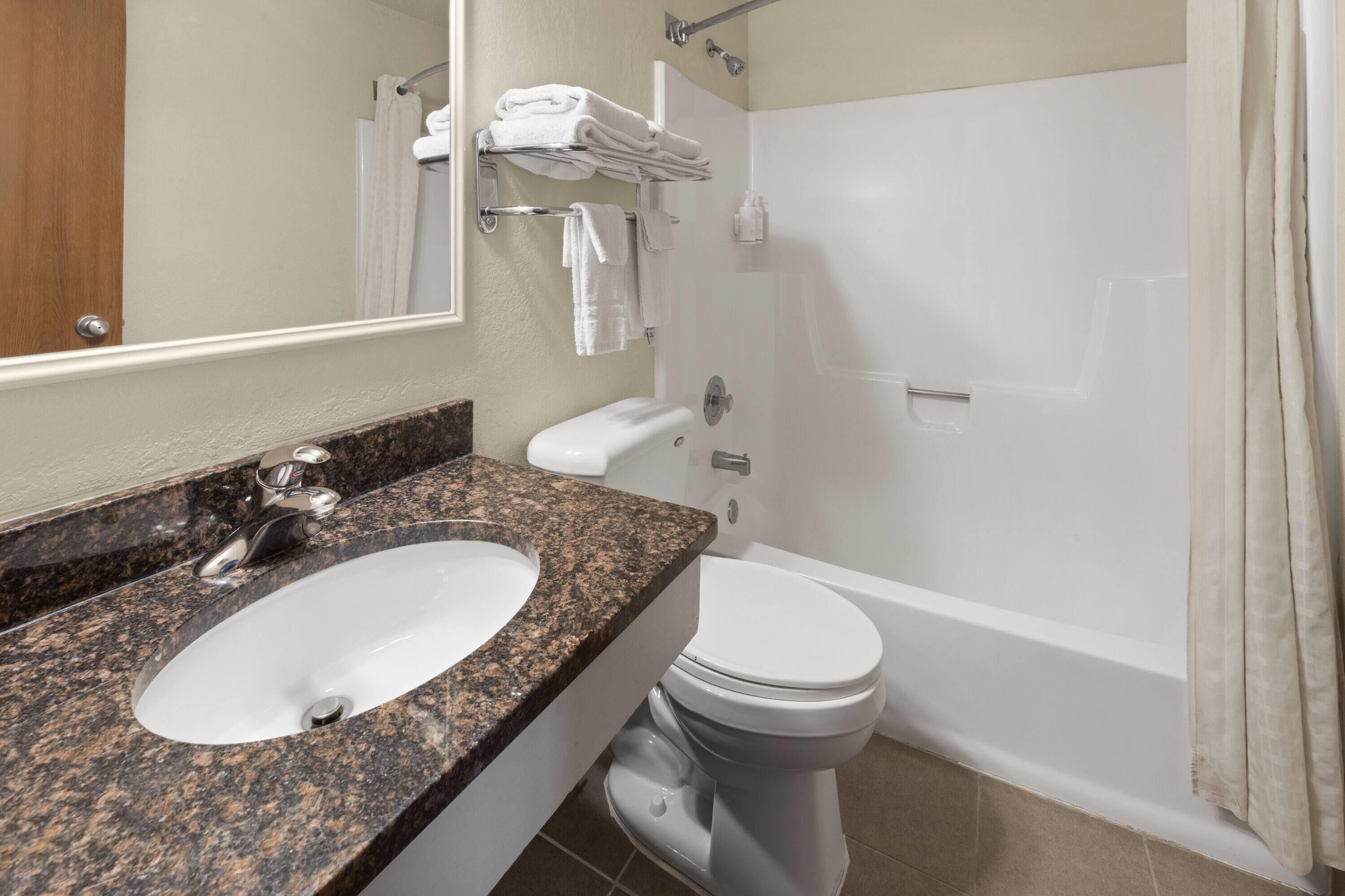 A bathroom with a granite countertop sink, white toilet, and a bathtub.
