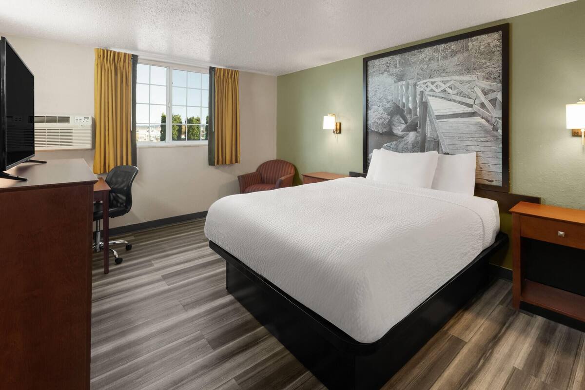 A hotel room with a large bed, a desk with a chair, a television, and a window with curtains.