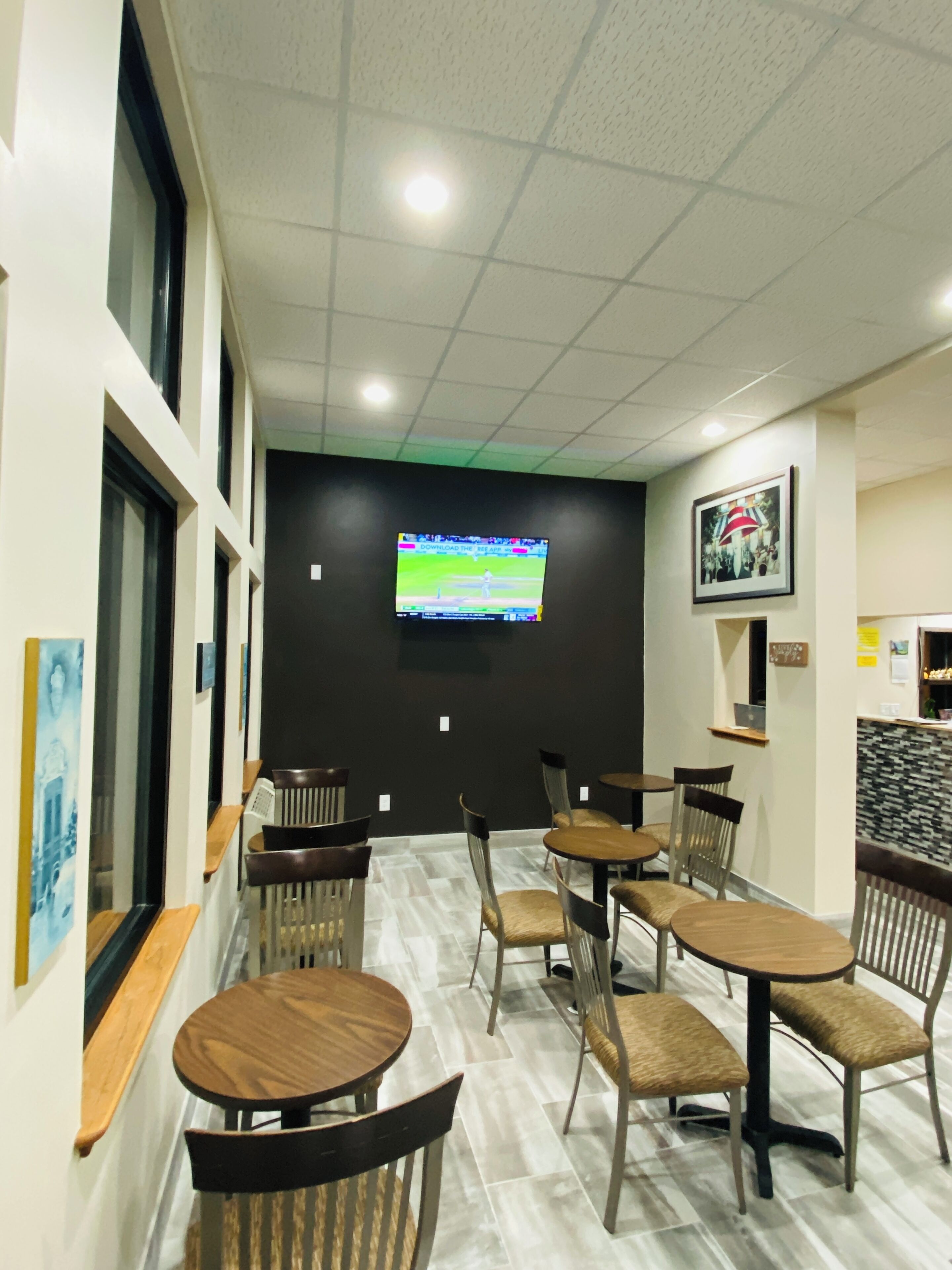 A modern restaurant interior with multiple tables and chairs, a large flat-screen TV mounted on the wall, and a framed picture above the counter.