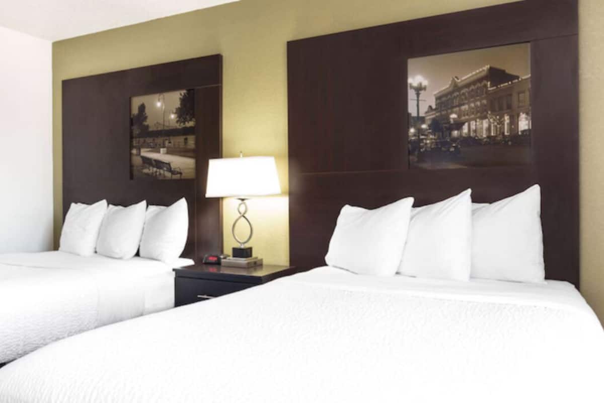 A hotel room with two beds, a nightstand with a lamp, and two framed pictures on the wall.