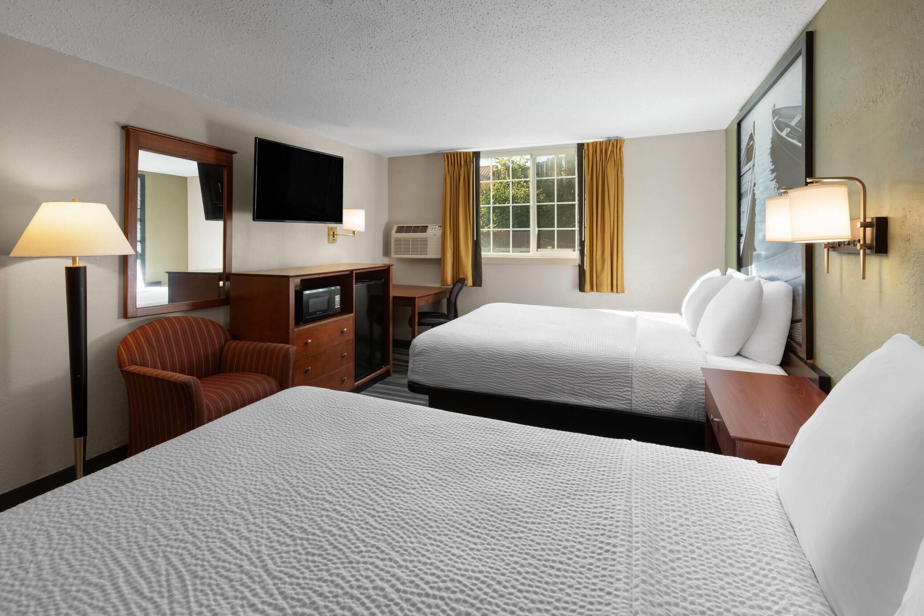 A hotel room with two beds, a desk, a chair, a TV, and a window with curtains.