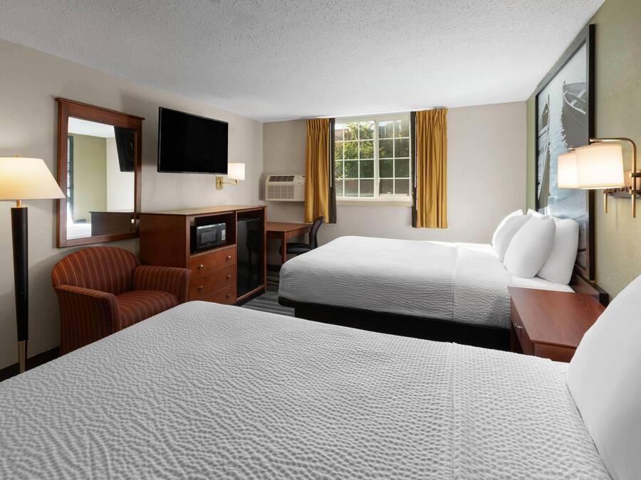 Une chambre d’hôtel avec deux lits, un bureau, une chaise, une télévision et une fenêtre avec des rideaux.