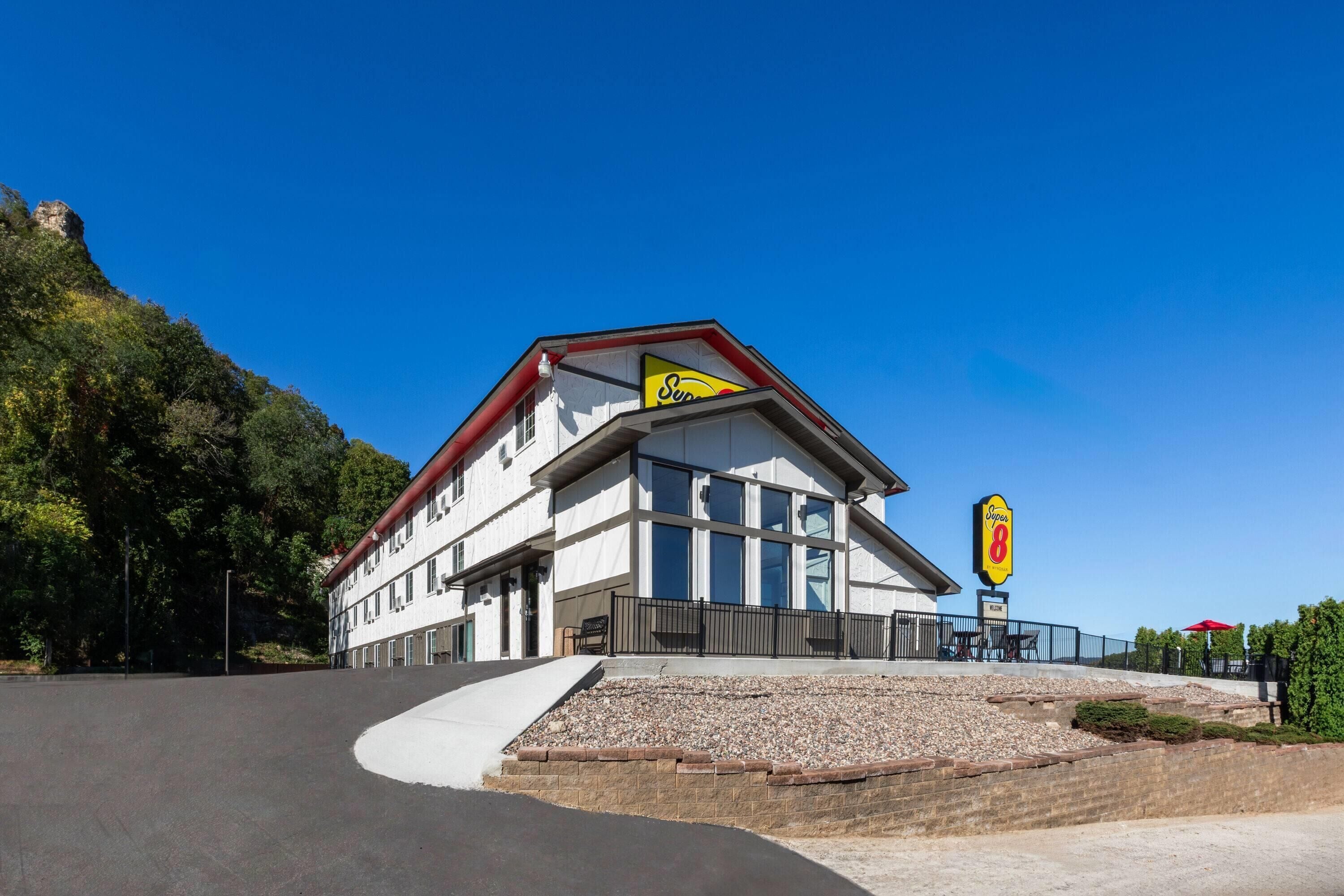 A hotel with a modern design, featuring a prominent 'Sun 8' sign, large windows, and a landscaped area with a paved path leading to the entrance.