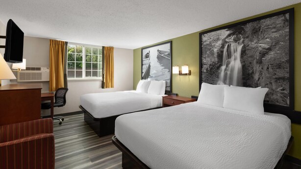 A hotel room with two beds, a desk with a chair, a TV, and a large waterfall painting on the wall. - Super 8 by Wyndham Winona MN (Winona)