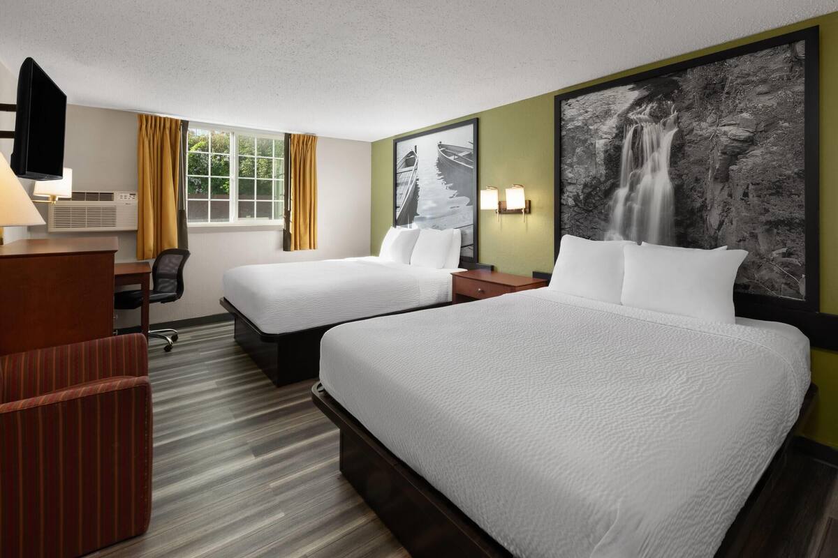 A hotel room with two beds, a desk with a chair, a TV, and a large waterfall painting on the wall.