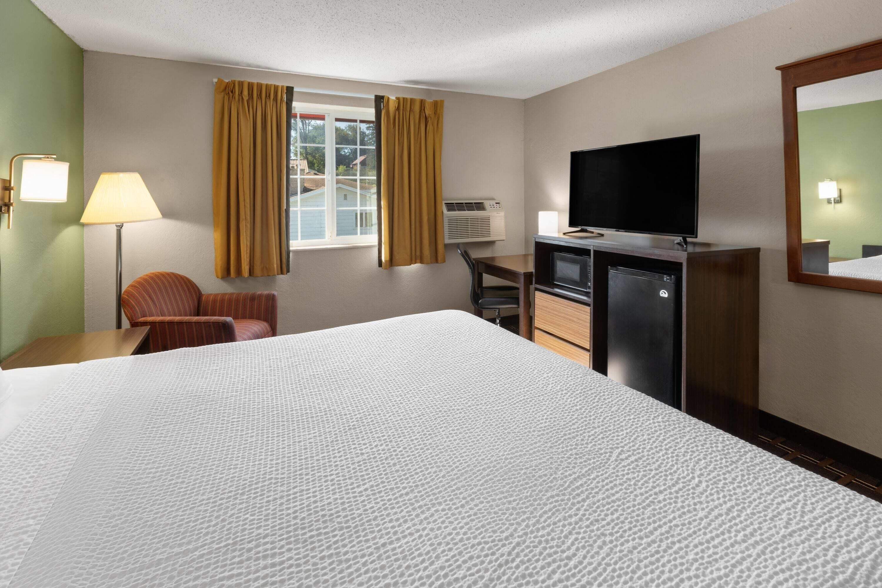 A hotel room with a large bed, a desk with a television, a chair, and a window with curtains.