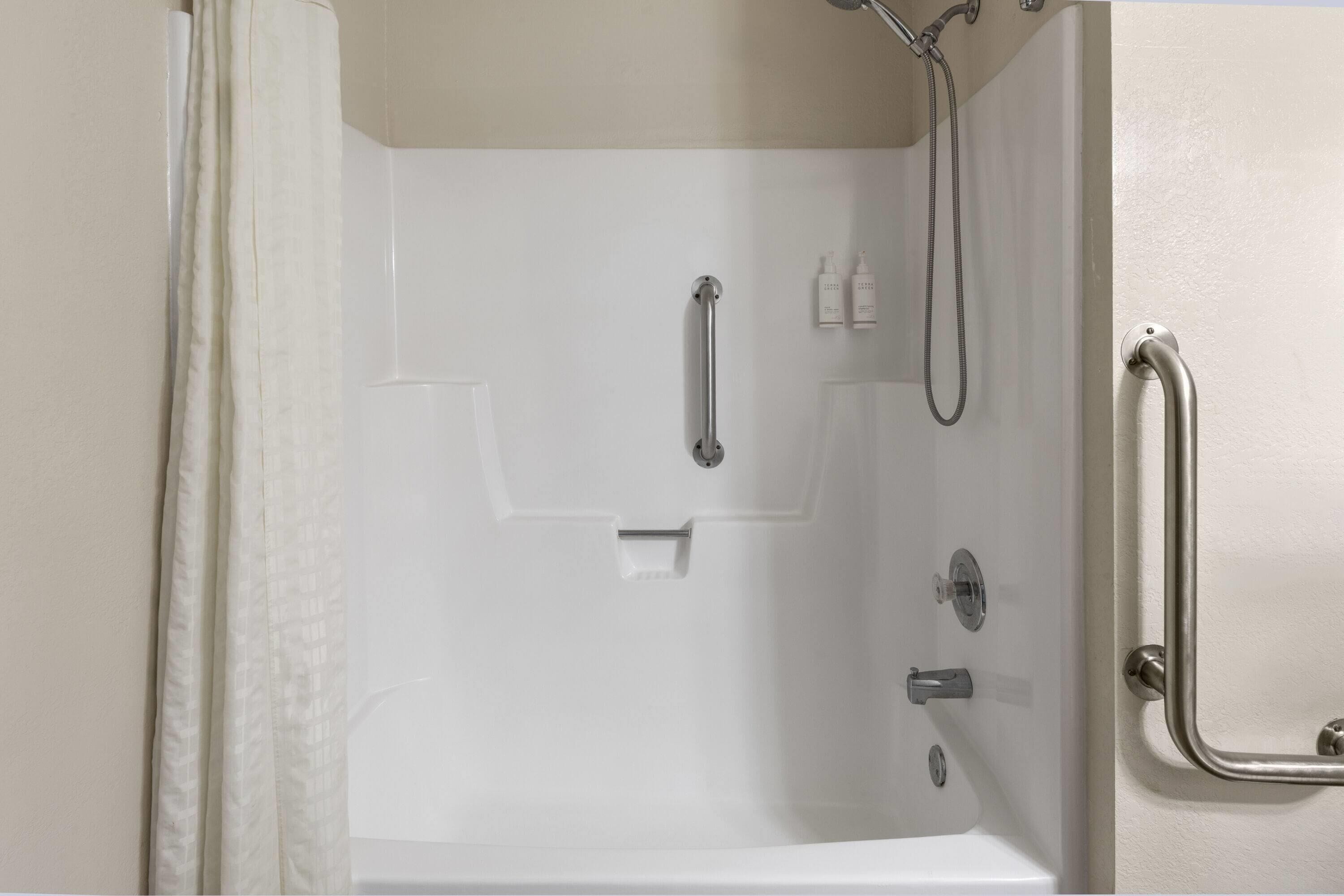 Ducha a nivel con bañera blanca, barras de apoyo y cabezal de ducha manual.