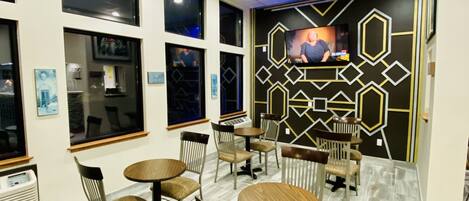 A modern interior with multiple round tables and chairs, a patterned wall design, and a television screen.