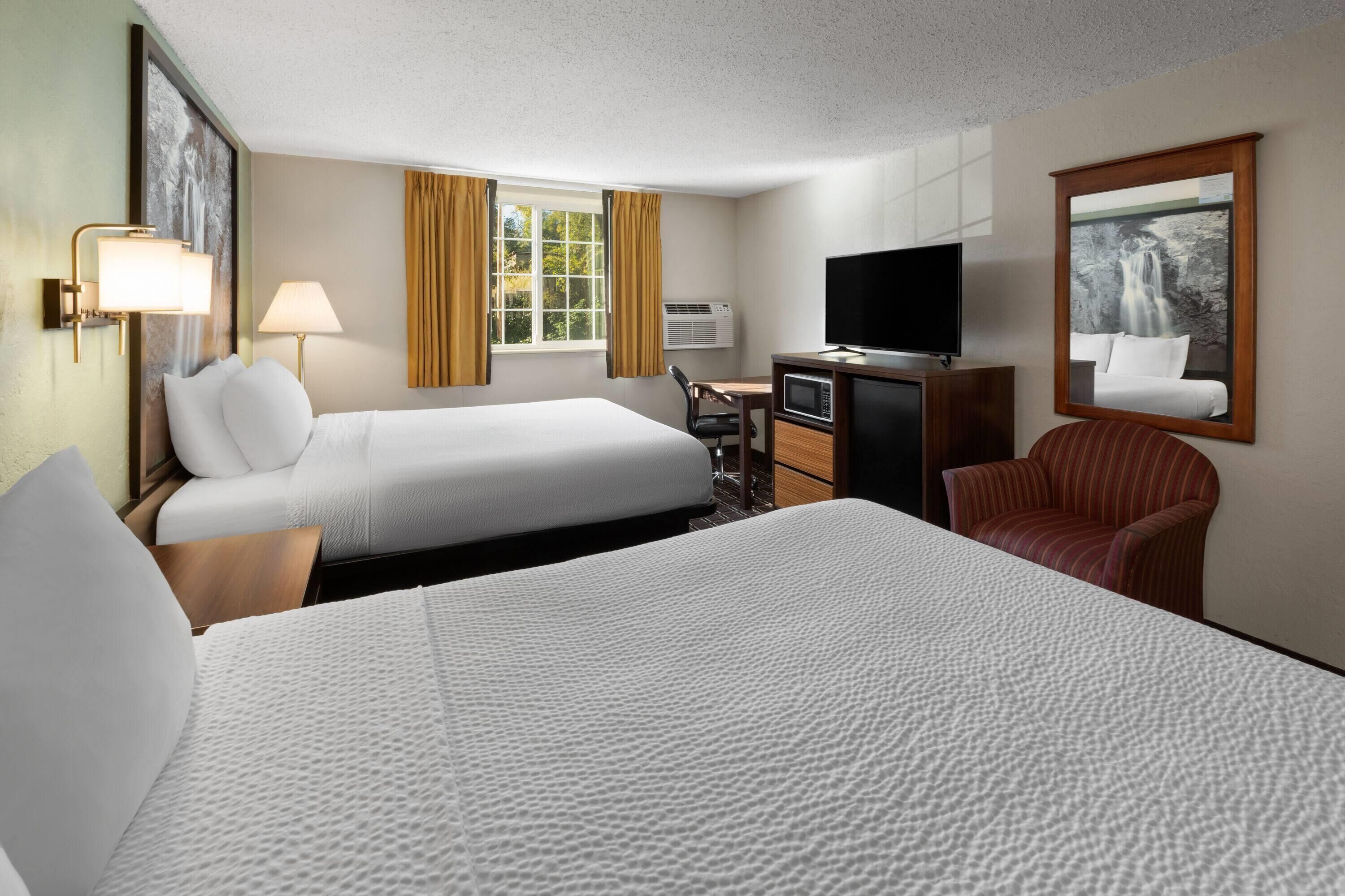 A hotel room with two beds, a desk with a TV, a chair, and a large window with curtains.