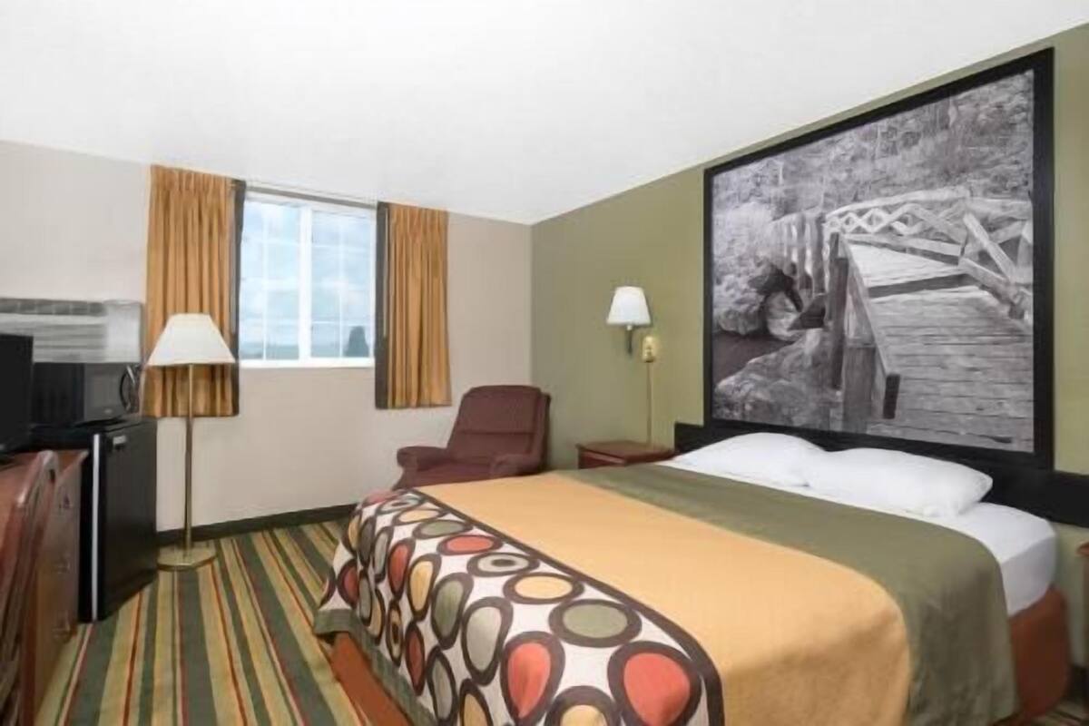 A hotel room with a bed, a desk, a chair, a television, and a painting on the wall.