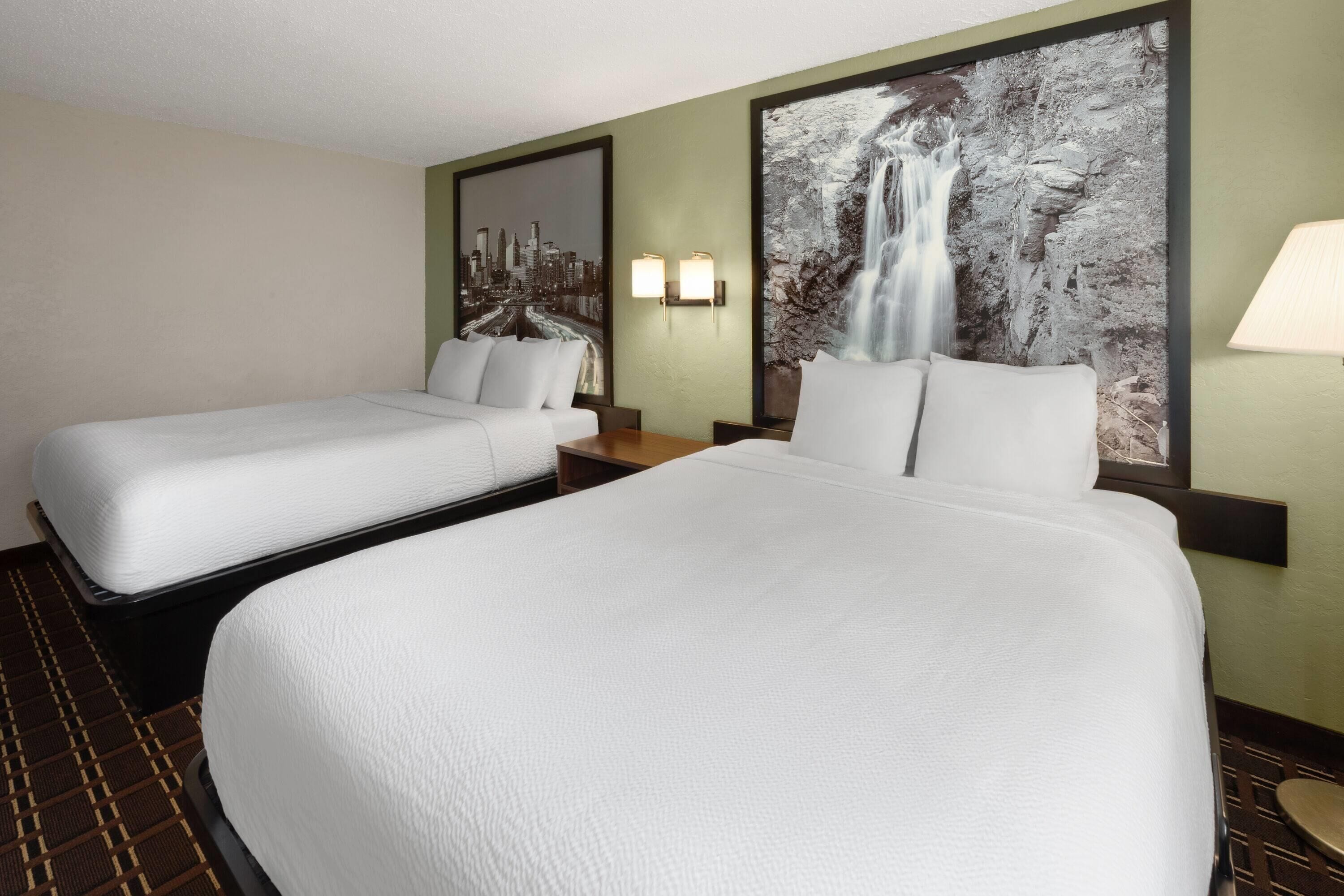 Een hotelkamer met twee eenpersoonsbedden, een groot bed, een stadslandschap schilderij, een waterval schilderij en een lamp.