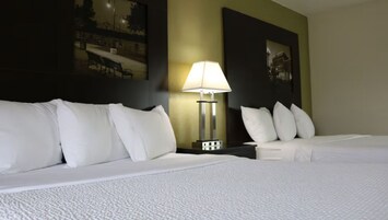 Una habitación de hotel con dos camas, una mesita de noche con lámpara y cuadros en la pared.