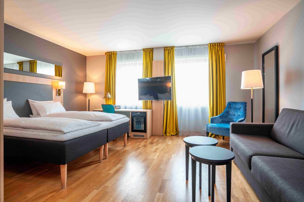 A hotel room with a bed, a sofa, a TV, and a desk with a lamp.