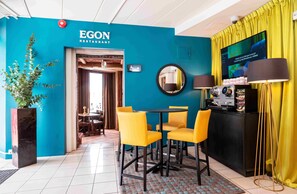 A restaurant interior with a teal wall, yellow chairs, a black table, and a TV screen. - Thon Hotel Lillestrøm (Lillestrom)