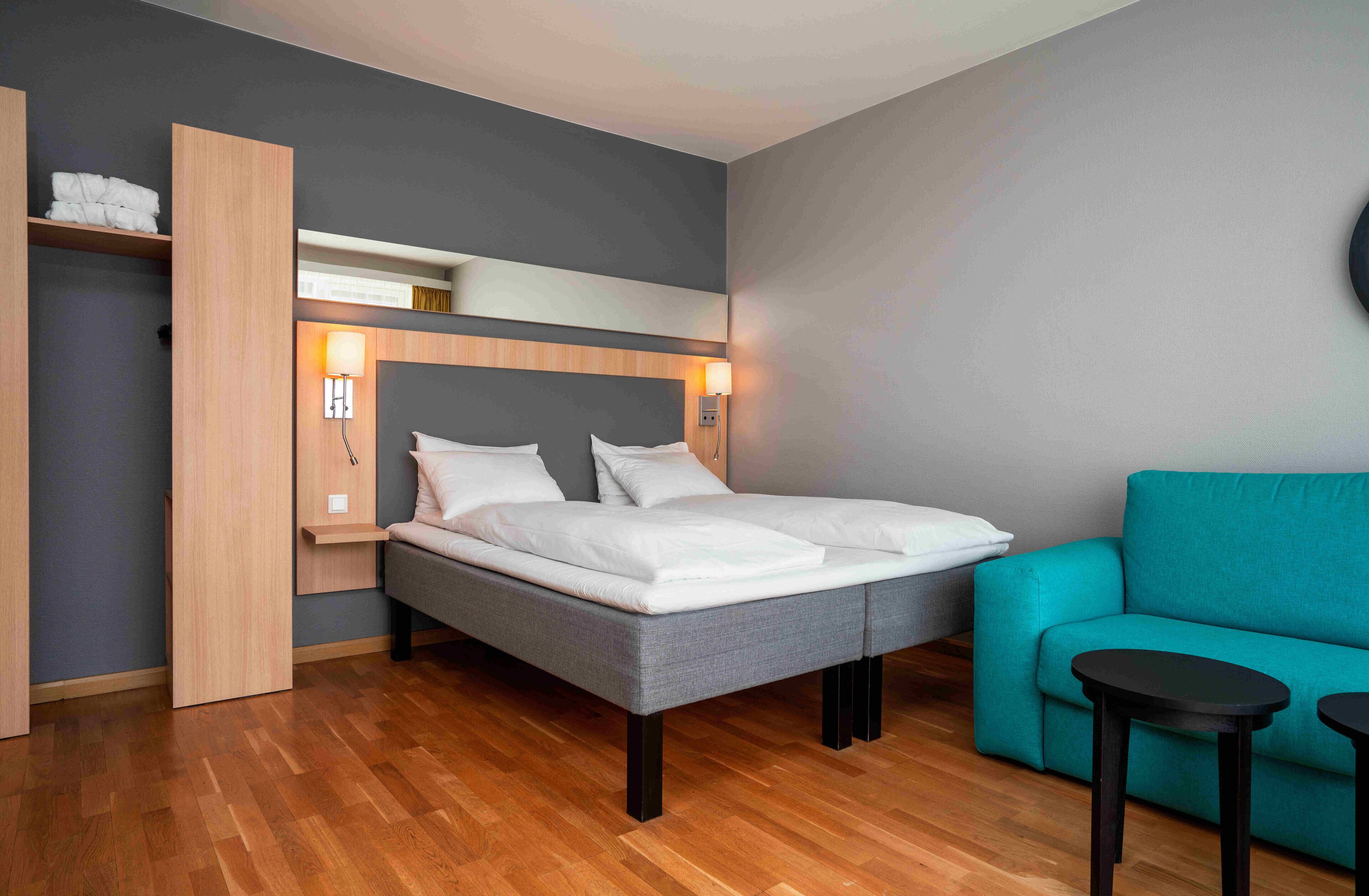 A modern hotel room with a large bed, a teal sofa, and two small tables.
