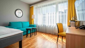 A hotel room with a bed, a teal sofa, a small table, a chair, a desk, a lamp, and a telephone. - Thon Hotel Lillestrøm (Lillestrom)