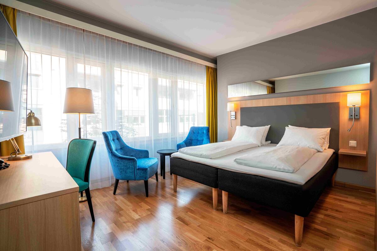 A hotel room with a bed, two chairs, a desk, and a lamp.