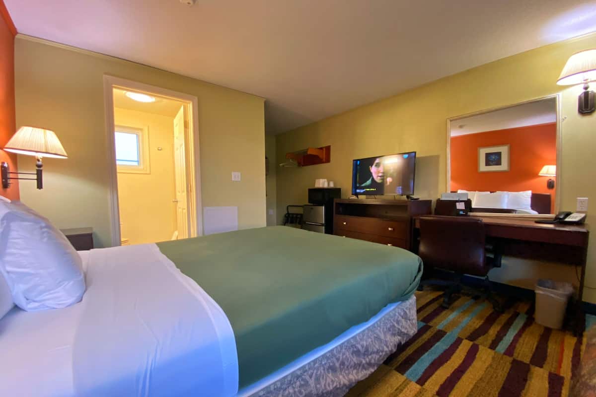 A hotel room with a bed, desk, chair, television, and a bathroom door.