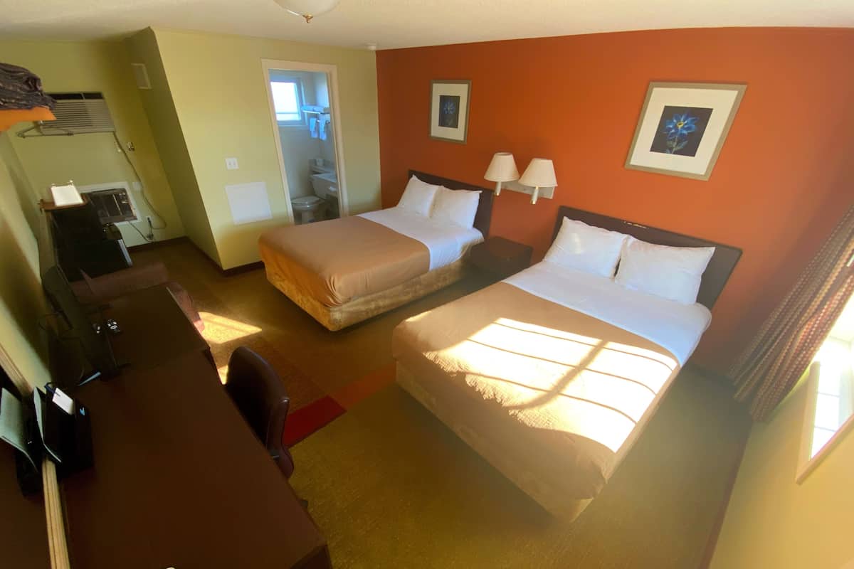 A hotel room with two beds, a desk, a chair, and a television.