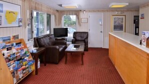 A room with a red carpet, two leather sofas, a wooden coffee table, a flat-screen TV, a wooden reception desk, and a magazine rack. - Best Stay Inn - Manchester (Manchester)