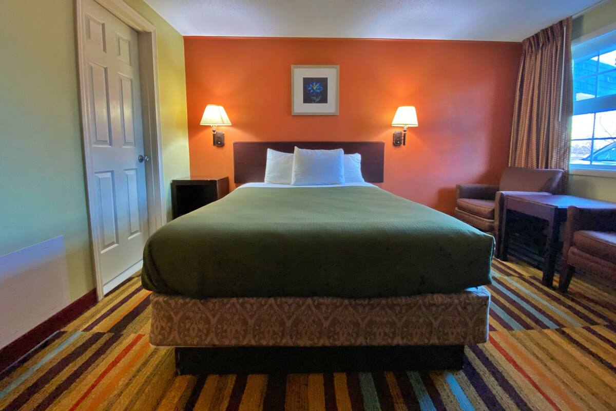 A hotel room with a bed, two bedside lamps, a chair, a desk, and a window with curtains.